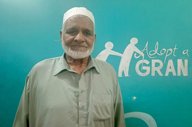 An elderly man standing in front of a teal background with the words 'Adopt a Gran', part of a Penny Appeal initiative supporting senior citizens