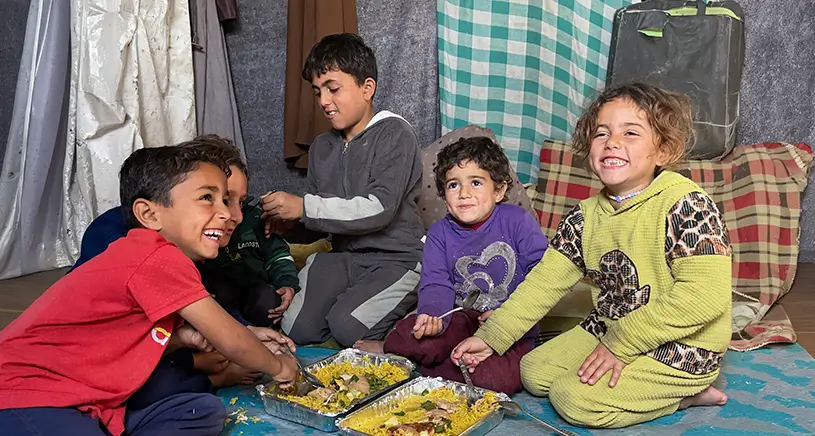 A group of children smile while eating a meal.
