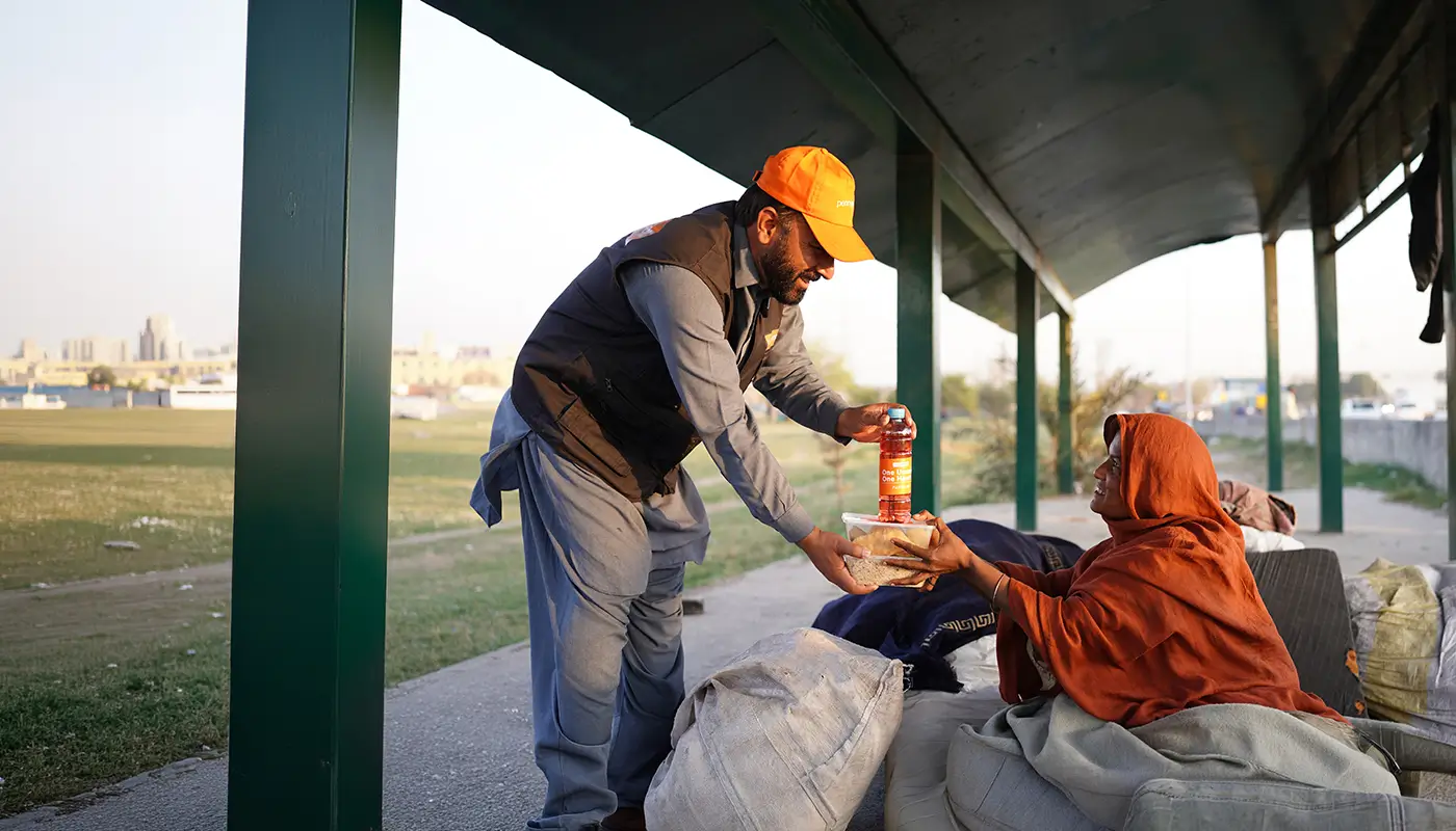 A Penny Appeal worker hands food and drink to a woman sat on the floor.