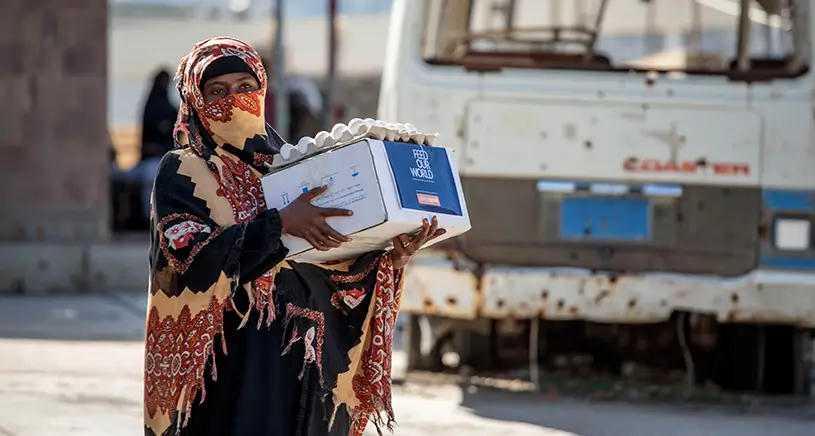 A lady in traditional clothing carried a box of food from Penny Appeal.