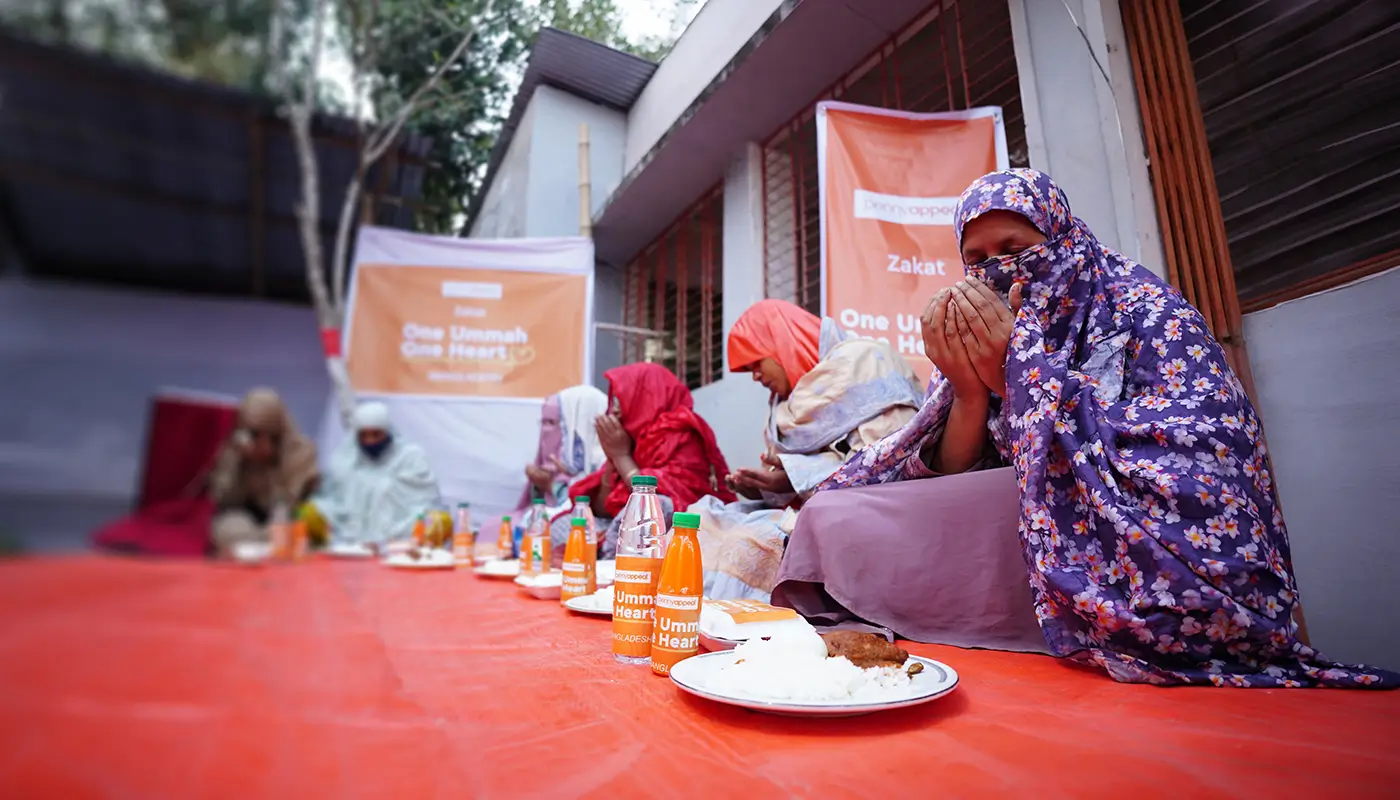 A group of people praying before receiving an iftar meal from Penny Appeal.