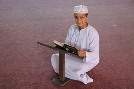 Boy kneeling and reading the Qur’an