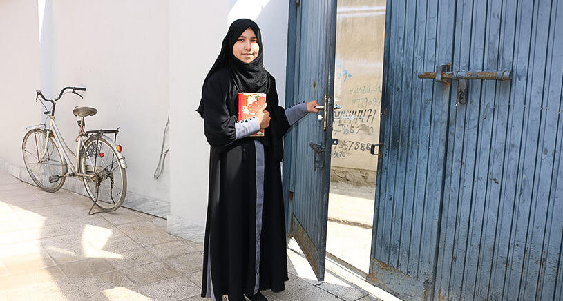 A girl in traditional black clothing smiles at the camera.