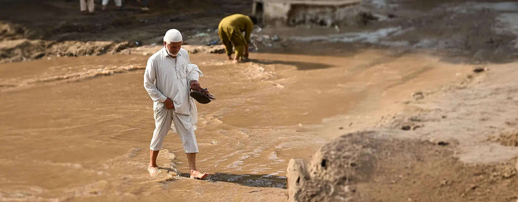 A man in white traditional clothing wades through water.