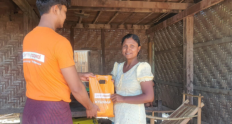 A man wearing a Penny Appeal t-shirt hands an orange Qurbani bag to a lady.