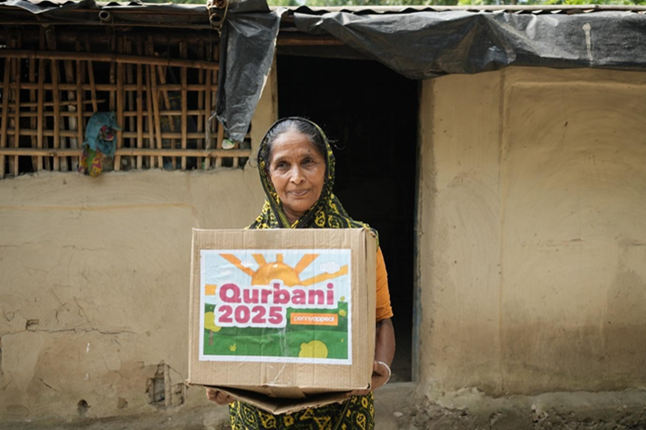 A woman holds a box labelled Qurbani 2025 Penny Appeal.
