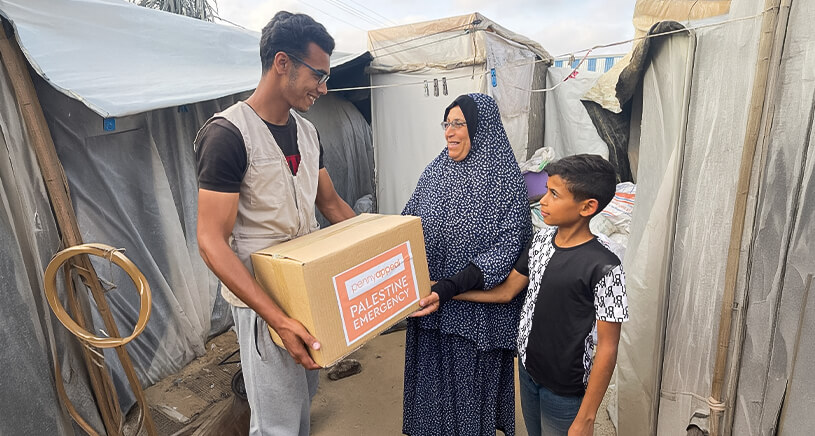 A smiling man hand a box of Penny Appeal supplies to a woman and a child.
