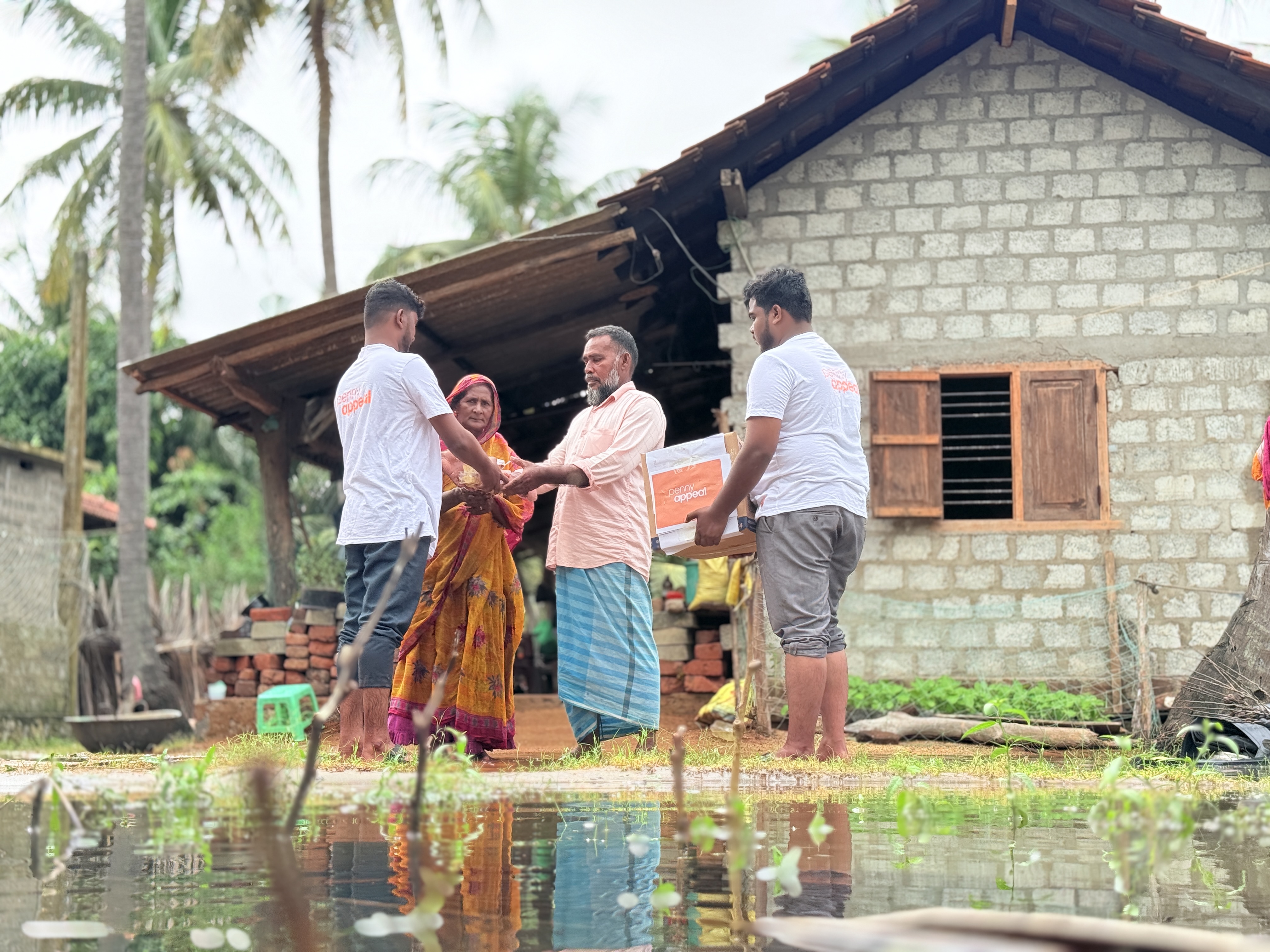 A family meet receive supplies from Penny Appeal workers outside of a home affected by flooding.