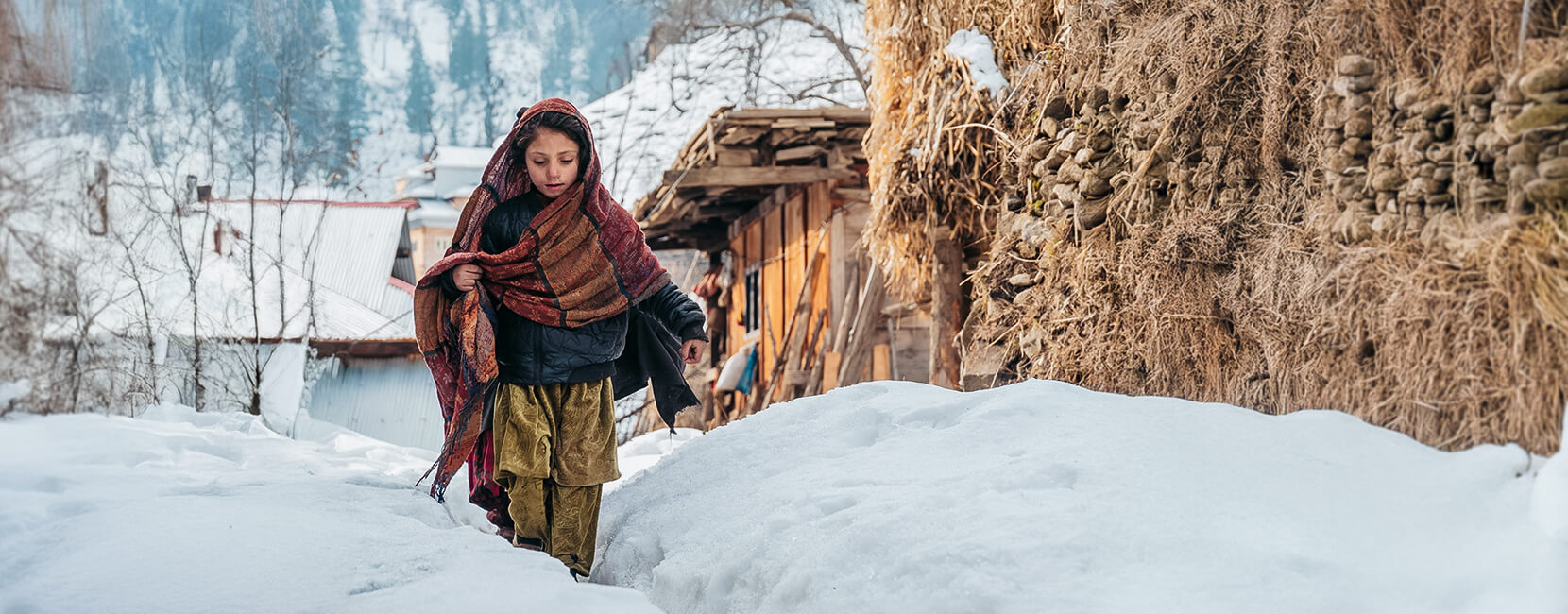 A child in traditional clothing walks through deep snow.