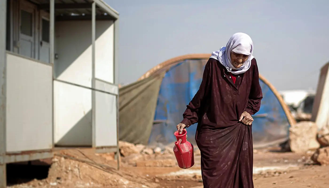 An elderly woman in traditional clothing walks through a displacement camp.