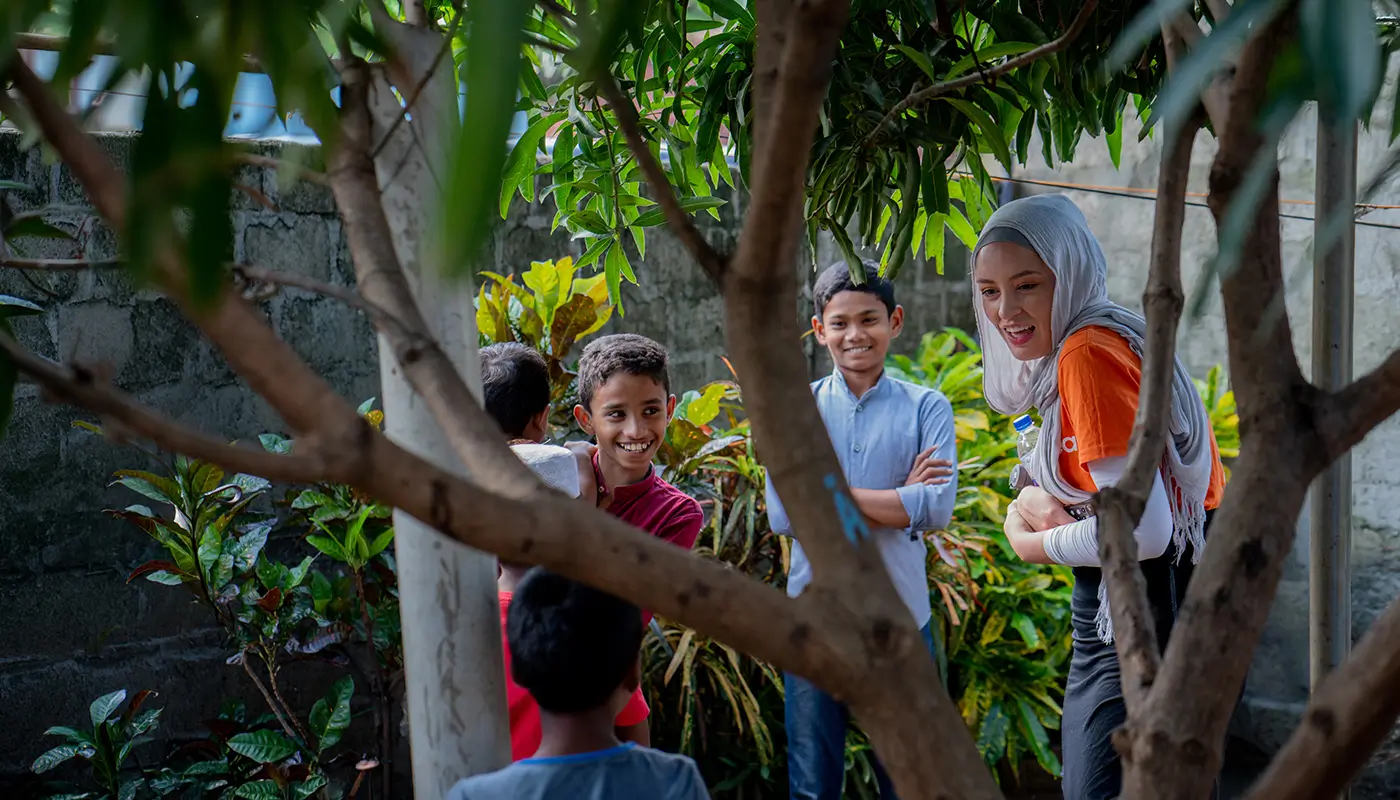 A Penny Appeal worker stands and chats with a group of smiling children.