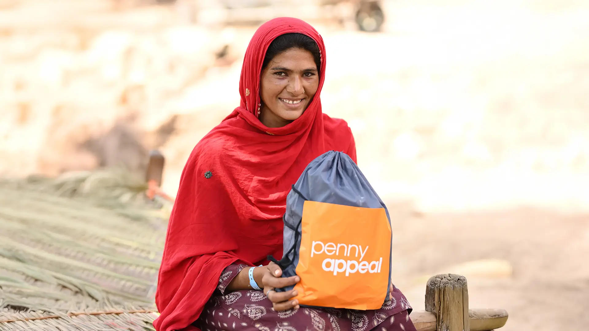A lady in traditional clothing sits with a Dignity Kit with Penny Appeal branding on her lap.