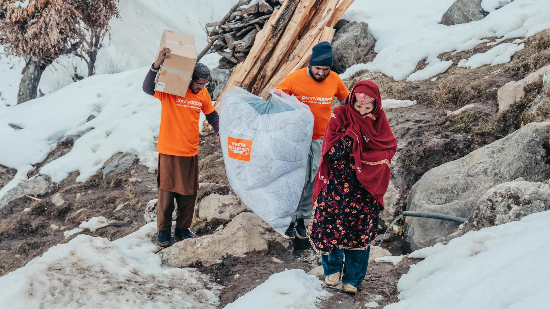 Penny Appeal volunteers deliver an Emergency Kit including winter supplies to a woman in a snowy mountain region, providing critical aid in harsh weather conditions.