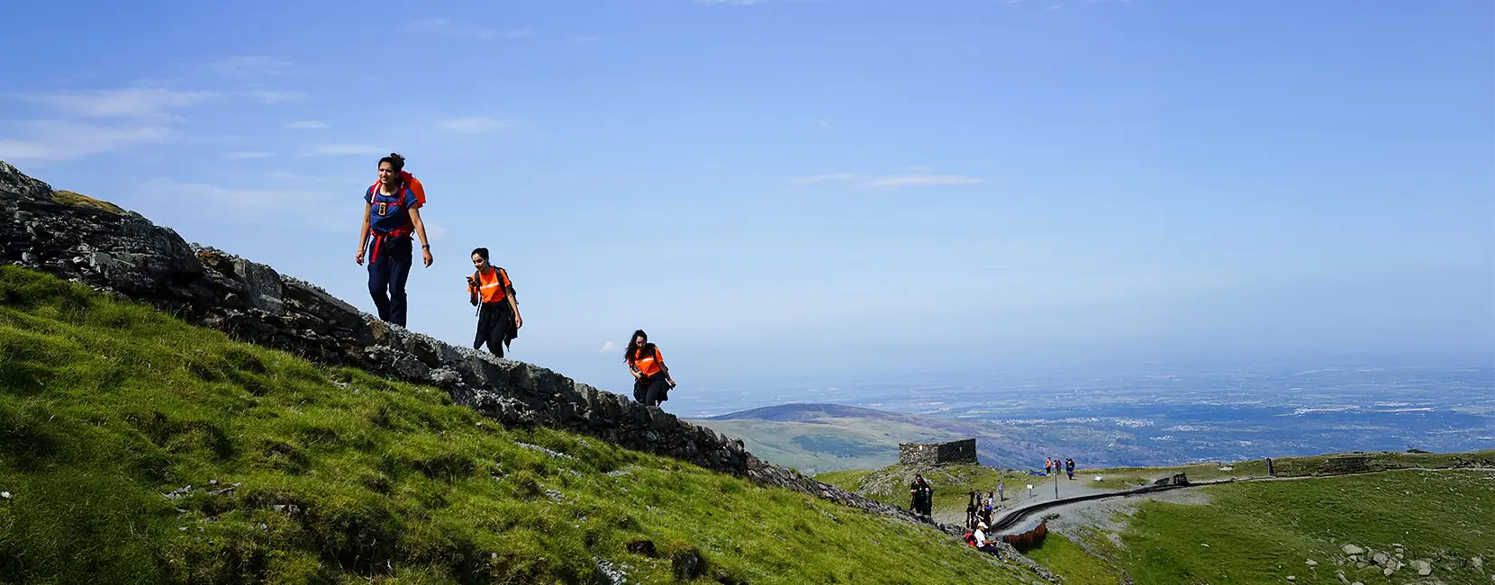 A community event organized by Penny Appeal called 'Eid in the Park,'' with people gathered around a stage featuring live performances under an orange canopy, surrounded by trees and urban buildings.